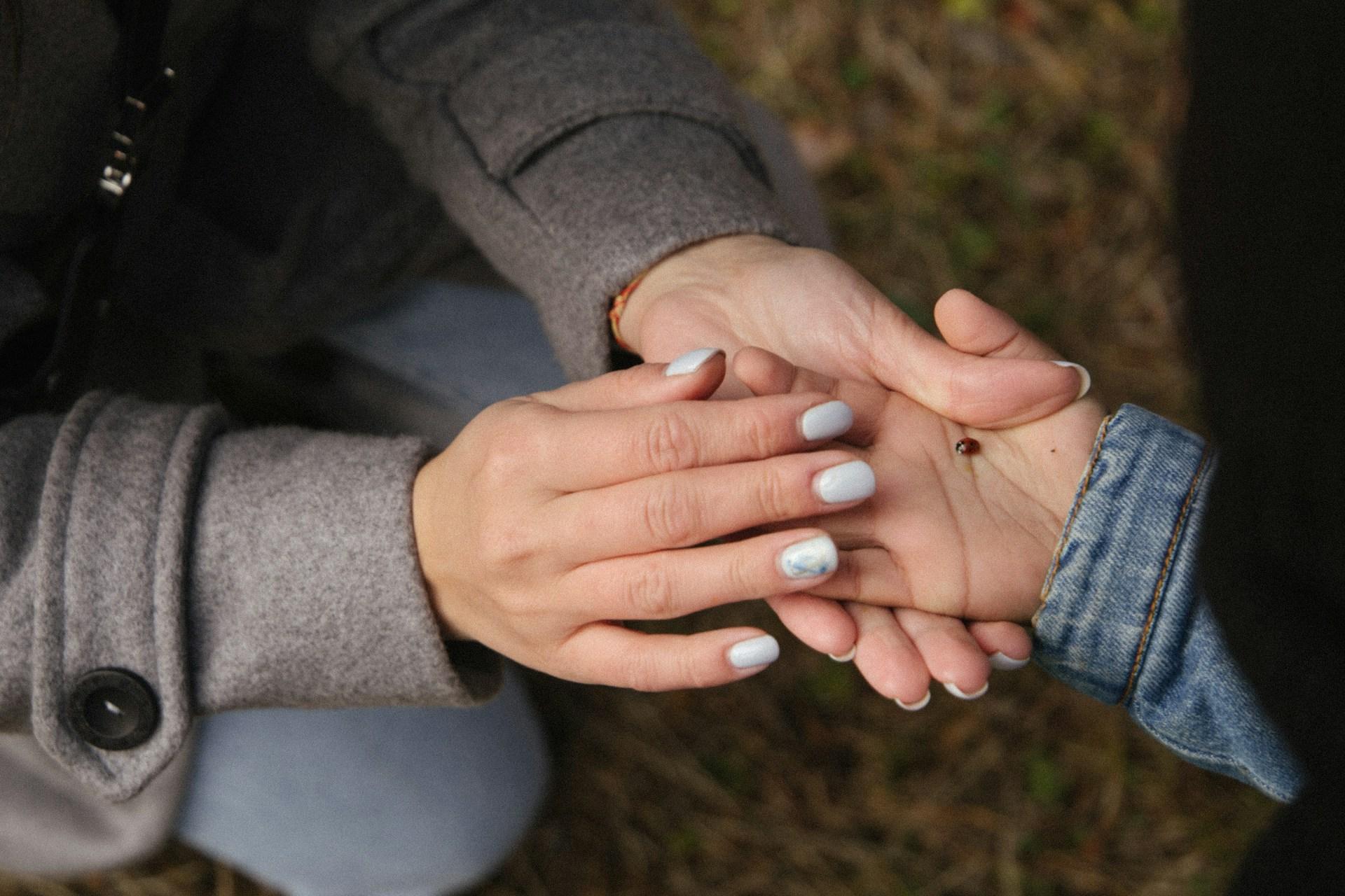 A mother gently holding her child's hand with a ladybug resting on the palm.