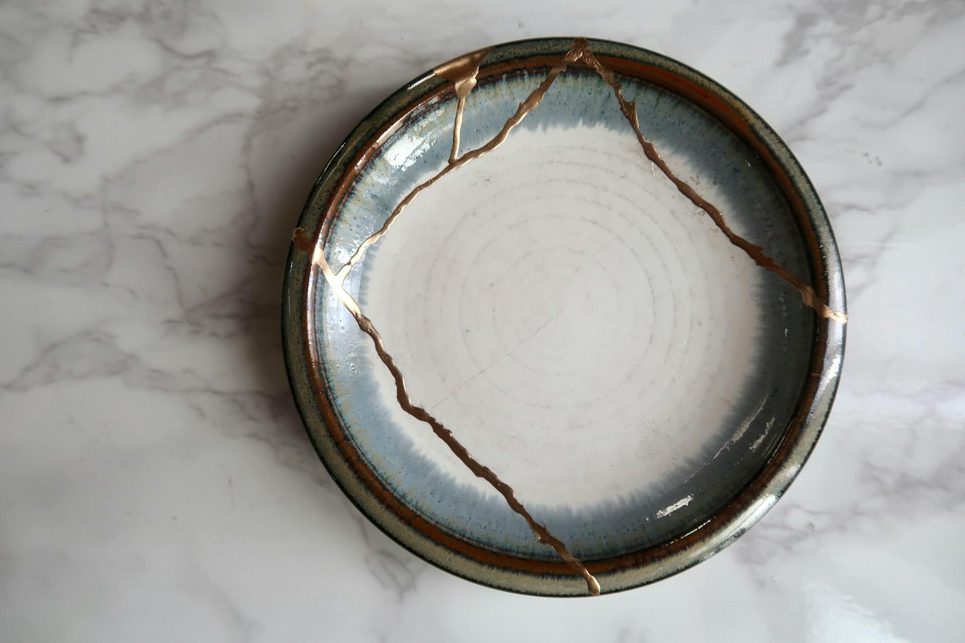 A repaired ceramic bowl with visible gold seams in the Japanese kintsugi style, symbolizing beauty in imperfection.